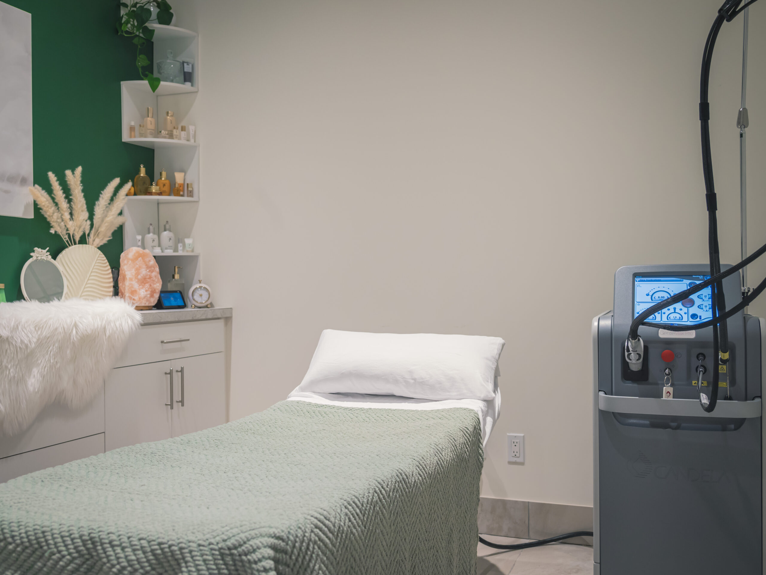 An image of a room with a single medical bed with a green blanket. to the right is the laser system used for hair removal